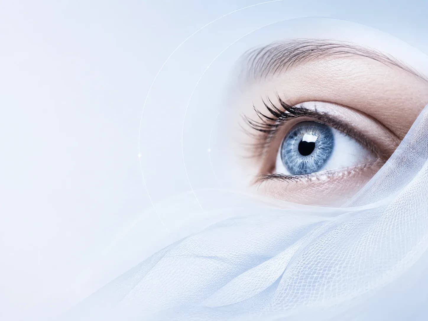 Close-up of a blue eye framed by soft, flowing fabric on a pale blue background